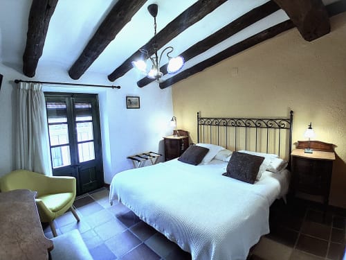 Dormitorio rústico en RuralGorgs B&B en El Vilosell con vigas de madera vista, cama de hierro, ropa de cama blanca y decoración de época