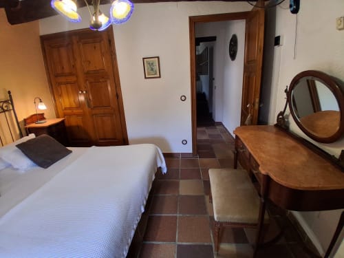 Acogedora habitación rural en RuralGorgs con cama blanca, muebles de madera, espejo redondo y piso de baldosa tierra cocida en El Vilosell