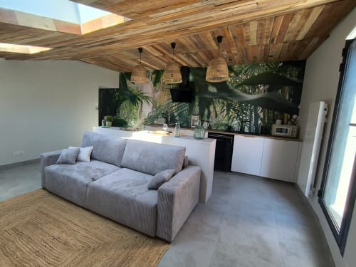 Studio moderne à Escale à Clisson avec canapé gris, kitchenette, plafond bois, plantes tropicales et vue sur la ville