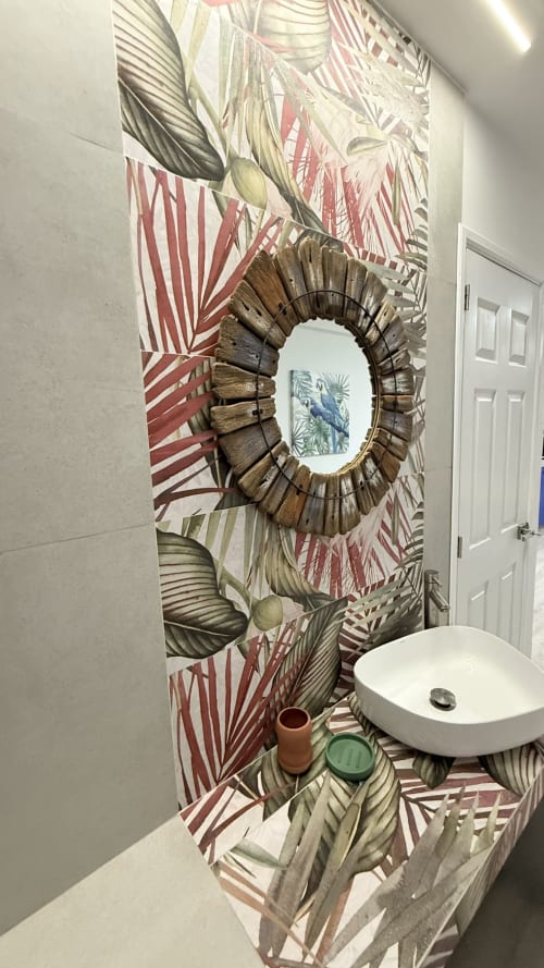 Tocador de baño con papel tapiz tropical decorativo, espejo de madera en forma de sol y lavamanos blanco en el apartamento Nautilus Palace