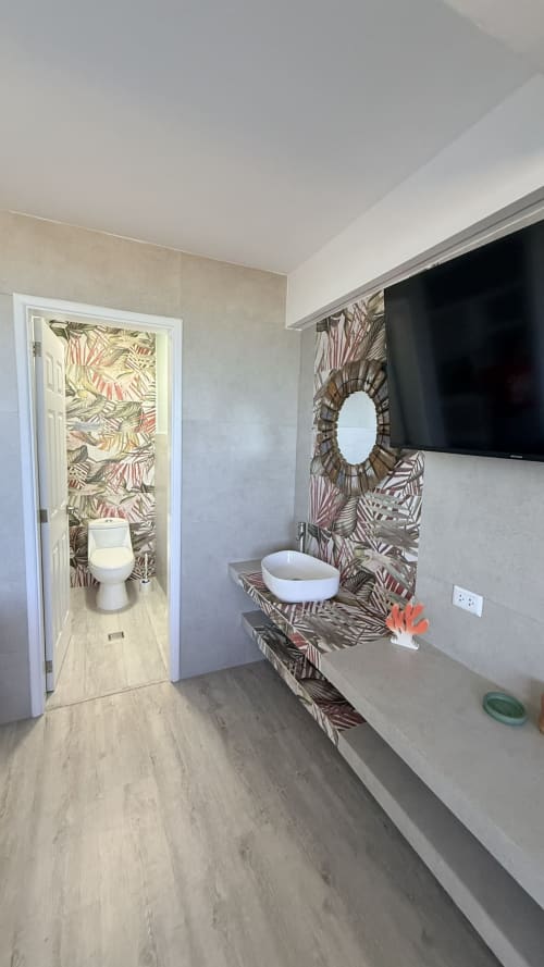 Baño moderno en apartamento Nautilus Palace Madrid con papel tapiz tropical, lavamanos blanco de cerámica, televisor de pared e inodoro