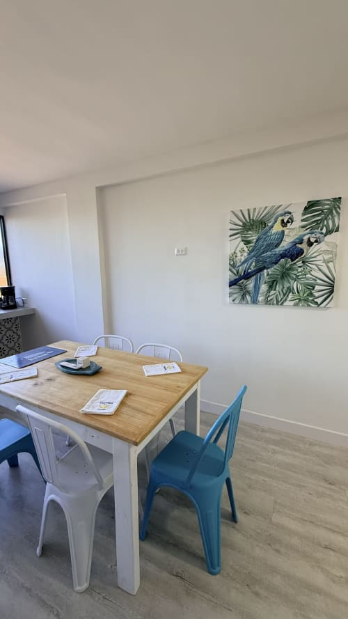 Comedor moderno en el apartamento Nautilus Palace, Madrid, con mesa de madera, sillas azules y cuadro de loro