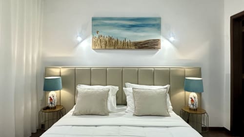 Quarto moderno com cabeceira acolchoada bege, roupa de cama branca, luminária teal e quadro paisagístico na Quinta das Susandas