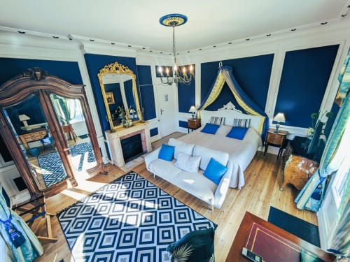 Luxueuse chambre du Château de Quesmy avec murs bleus, lit à baldaquin, miroir orné et mobilier élégant