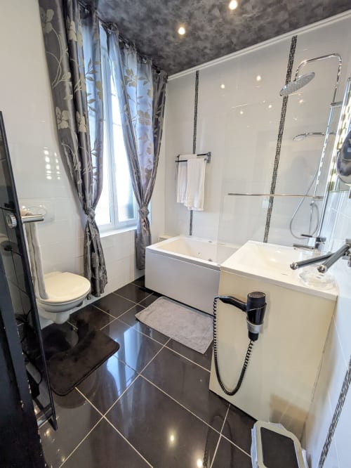 Salle de bain moderne de la Chambre Saphir au Château de Quesmy avec sanitaires blancs, sol en carrelage foncé, douche à l'italienne et fenêtre