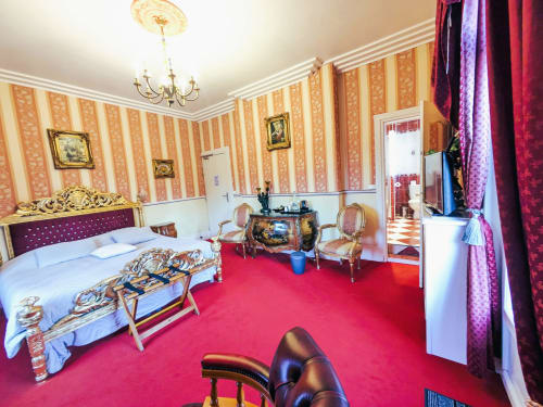 Chambre Rubis élégante au Château de Quesmy avec papier peint rayé, tapis rouge, mobilier raffiné et vue sur le jardin