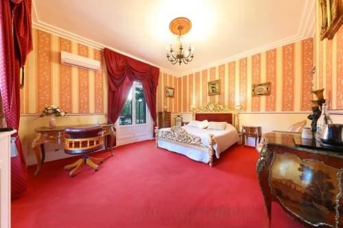 Chambre rouge luxueuse au Château de Quesmy avec papier peint rayé, mobilier orné et vue sur le jardin