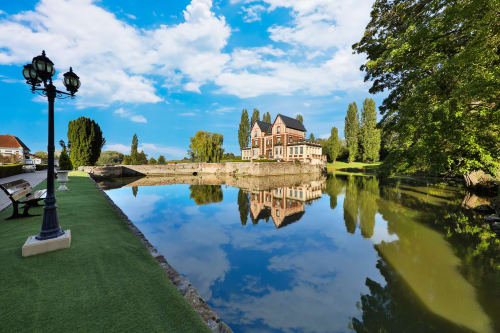 Château de Quesmy se reflétant dans un canal tranquille avec jardins soignés et peupliers à Quesmy, France
