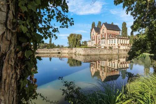 Château de Quesmy reflété dans une eau tranquille, murs de pierre couverts de lierre et peupliers, QUESMY