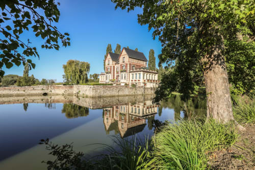 Le Château de Quesmy se reflète dans une eau calme, un manoir victorien entouré d'arbres verdoyants et de jardins soignés à Quesmy