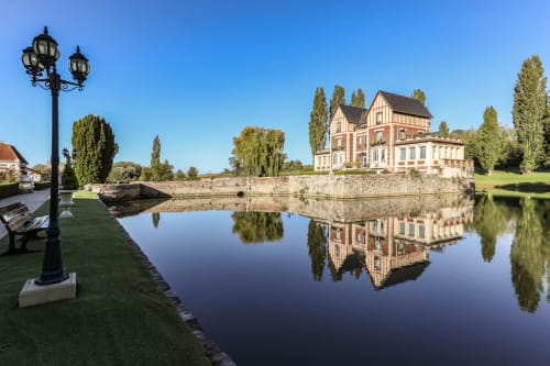 Château de Quesmy reflété dans l'eau calme, avec jardins entretenus et peupliers sous un ciel bleu