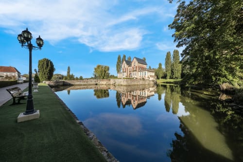 Chateau de Quesmy reflected in calm moat waters with manicured gardens and period architecture
