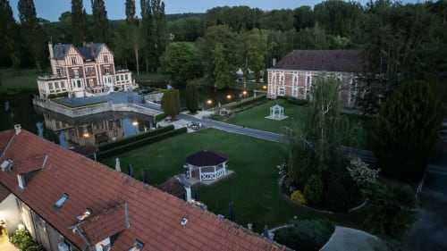 Domaine du Château de Quesmy en France avec son mansion illuminée, jardins soignés et parc élégant au crépuscule