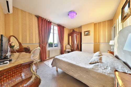 Chambre élégante au Château de Quesmy avec mobilier d'époque, literie crème, rideaux rouges et vue sur le jardin