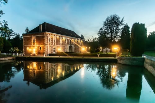 Château de Quesmy illuminé au crépuscule, reflété dans l'eau calme du canal avec jardins et arbres soignés, Quesmy France