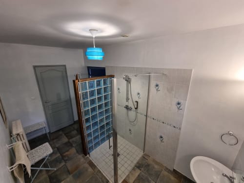 Modern bathroom with glass shower enclosure, decorative blue tiles, and bright blue pendant light at Manoir De La Maison