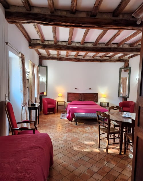 Chambre spacieuse au Manoir de la Maison Blanche avec poutres apparentes, literie rose, fauteuils rouges et carrelage terre cuite