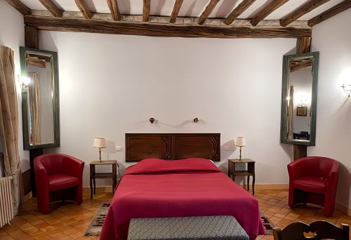Elegant bedroom at Manoir De La Maison Blanche in Amboise with red bed, wooden beams, mirrors, and burgundy armchairs