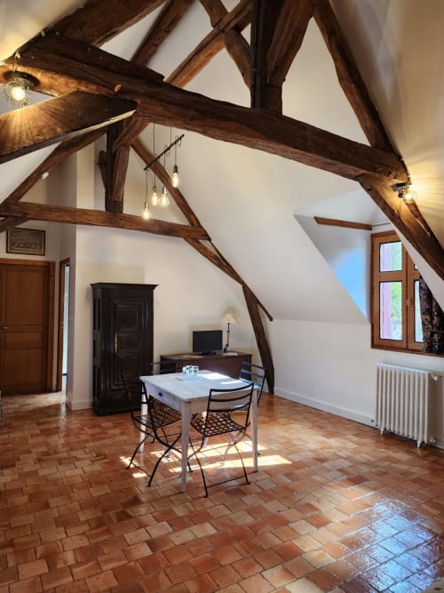 Camera da letto luminosa in soffitta con travi in legno a vista, tavolo da pranzo, scrivania e vista sul giardino al Manoir De La Maison Blanche, Amboise