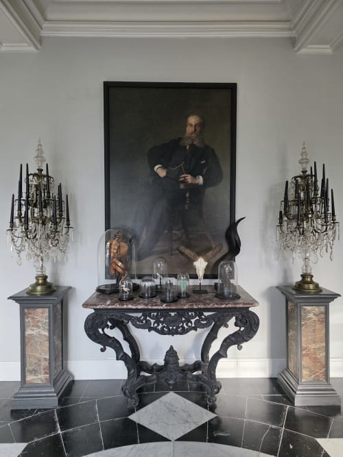 Elegant hallway at Castanea Business & Suites with ornate black console table, crystal candelabras, and classical portrait