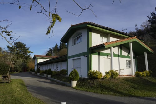 Apartamento dúplex Bizkar Bare en Vizcaya con arquitectura blanca y verde, entorno montañoso y entrada pavimentada