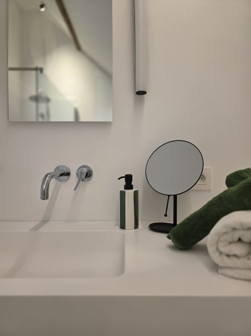 Modern bathroom vanity at Castanea Business & Suites with chrome faucet, soap dispenser, round mirror, and green towels