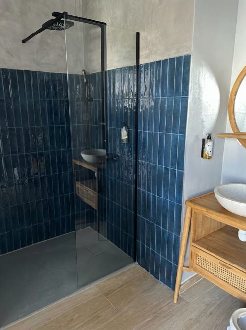 Modern bathroom with dark blue tile shower enclosure, black fixtures, wooden vanity, and white sink basins at Hôtel du Pont