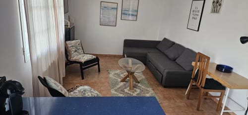 Elegante sala de estar del hotel Bizkar Bare en Vizcaya con sofá oscuro, mesa de cristal redonda, sillas de madera y jardín