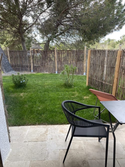 Private garden patio at Hôtel du Pont Blanc with black chair, lush green lawn, and rustic wooden fence in