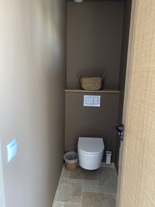 Modern toilet room with white ceramic toilet, woven storage baskets, and dual light switches at Hôtel du Pont Blanc in