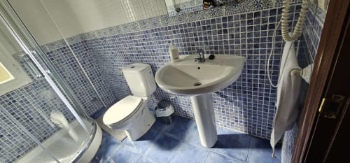 Baño moderno del hotel Bizkar Bare en Vizcaya con lavabo de pedestal, inodoro, ducha y azulejos mosaico azules