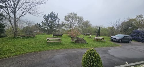 Vista del jardín en Bizkar Bare, Vizcaya, con mesas de picnic, césped verde, coche aparcado y árboles