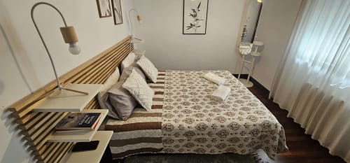 Moderno dormitorio en el hotel Bizkar Bare de Vizcaya con cama de madera, ropa de cama estampada, lámpara de arco y ventanas con vistas al jardín