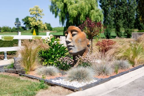 Sculpture en bronze entourée de graminées ornementales dans le jardin du Château de Quesmy avec croix et arbres