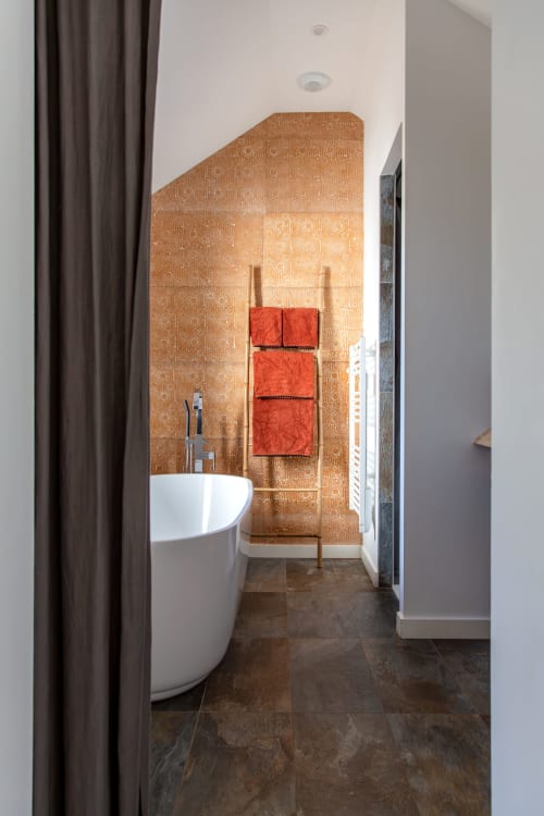 Modern spa bathroom at Villa Figue Blanche with freestanding tub, copper tile wall, and red towel ladder in