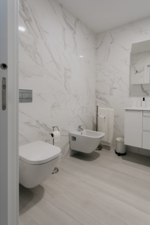 Baño moderno con paredes de mármol blanco, inodoro, bidé, lavabo y tocador en el apartamento Casa Lumar en Sesimbra, Portugal