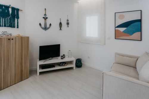 Salón moderno de Casa Lumar en Sesimbra con sofá beige, televisión, almacenamiento de madera, decoración náutica y arte abstracto