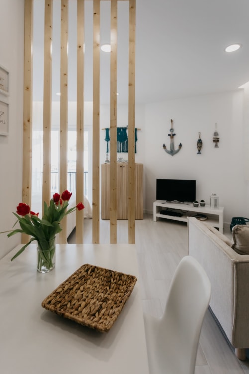 Cocina y sala de estar modernas en Sesimbra con divisor de lamas de madera, tulipanes rojos, cesto tejido y televisor