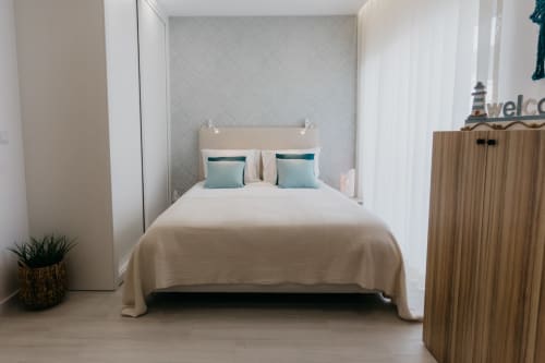 Dormitorio moderno en el apartamento Casa Lumar, Sesimbra Sun Sea, con ropa de cama crema, almohadas turquesas y armario de madera
