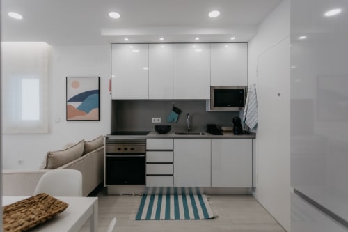 Cocina moderna con armarios blancos, encimera negra, estufa y zona de comedor en el apartamento Casa Lumar, Sesimbra