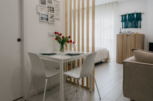 Comedor moderno con mesa blanca, sillas, tulipanes rojos, biombo de madera y sala de estar costera en Sesimbra