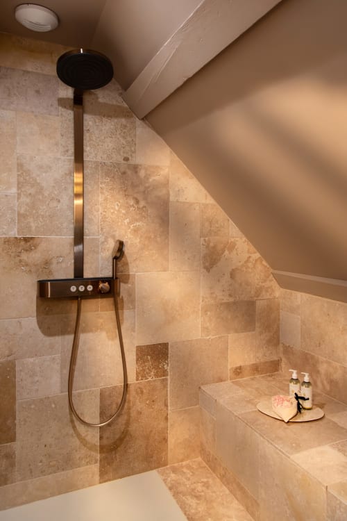 Salle de bain luxueuse à la Villa Figue Blanche avec carrelage en travertin, douche à effet pluie et accessoires noirs modernes