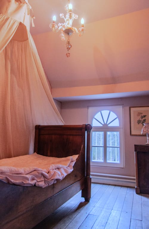 Elegant bedroom at Castanea Suites in Merelbeke with canopy bed, crystal chandelier, and garden view doors