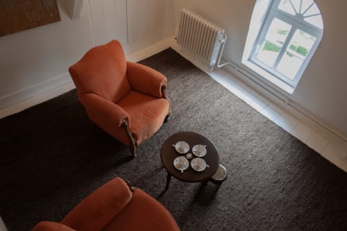 Thérèse Suite lounge area at Castanea Business & Suites with orange armchair, dark round table, and arched window in