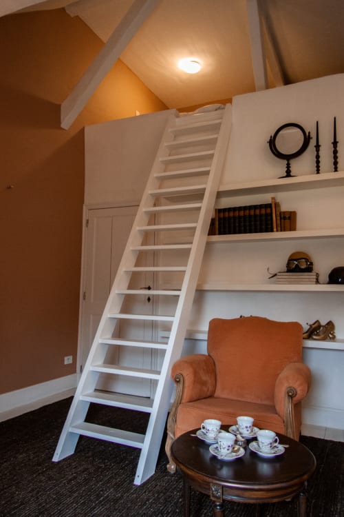 Thérèse Suite at Castanea Business & Suites featuring orange accent wall, white shelving with books, orange armchair, and