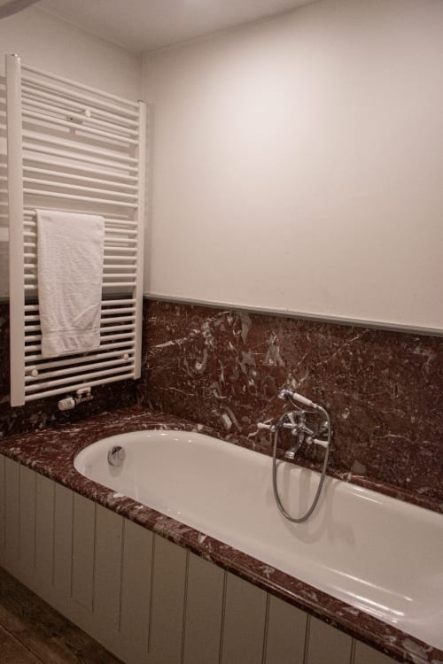 Luxury bathtub with dark marble surround and white towel rack in Thérèse Suite at Castanea Business & Suites, Merelbeke