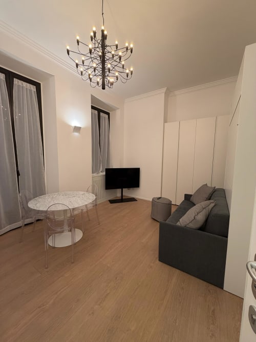 Modern studio apartment at Maisons Milano with seating area, TV, dining table, and elegant chandelier