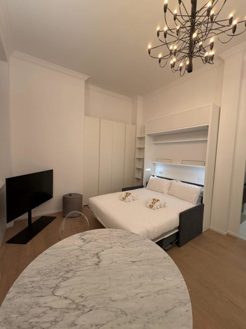Modern studio apartment at Maisons Milano with queen bed, marble table, TV, and built-in wardrobes in white minimalist design
