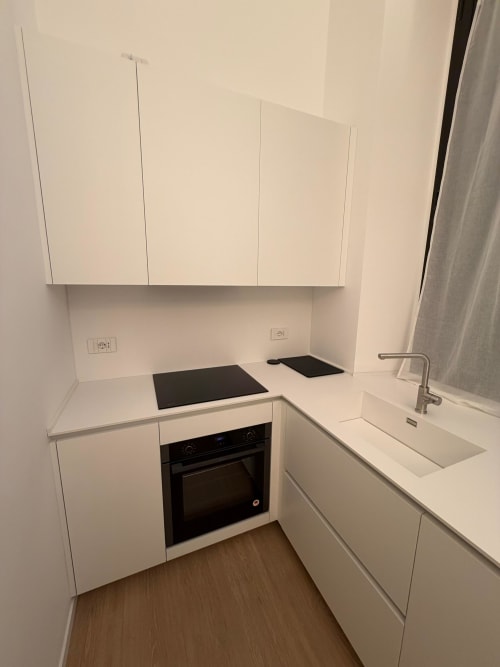 Modern white kitchen in Maisons Milano apartment with built-in oven, cooktop, and sink in Milan