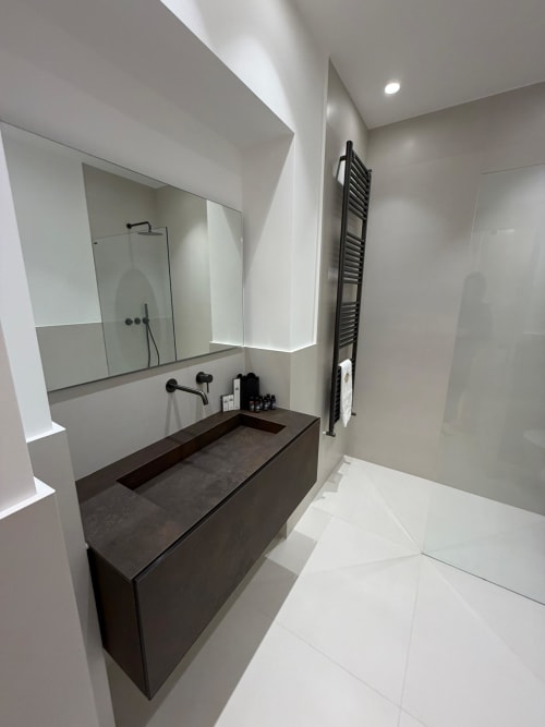 Modern bathroom at Maisons Milano with dark vanity sink, large illuminated mirror, walk-in shower, and heated towel rack
